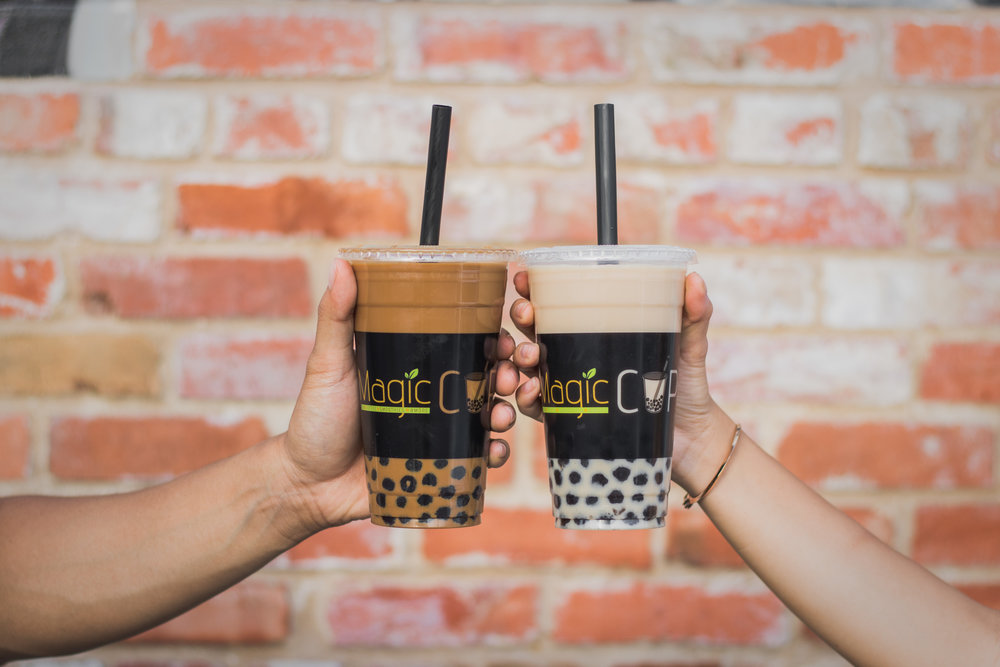 Two individuals holding up and tapping their milk tea with boba